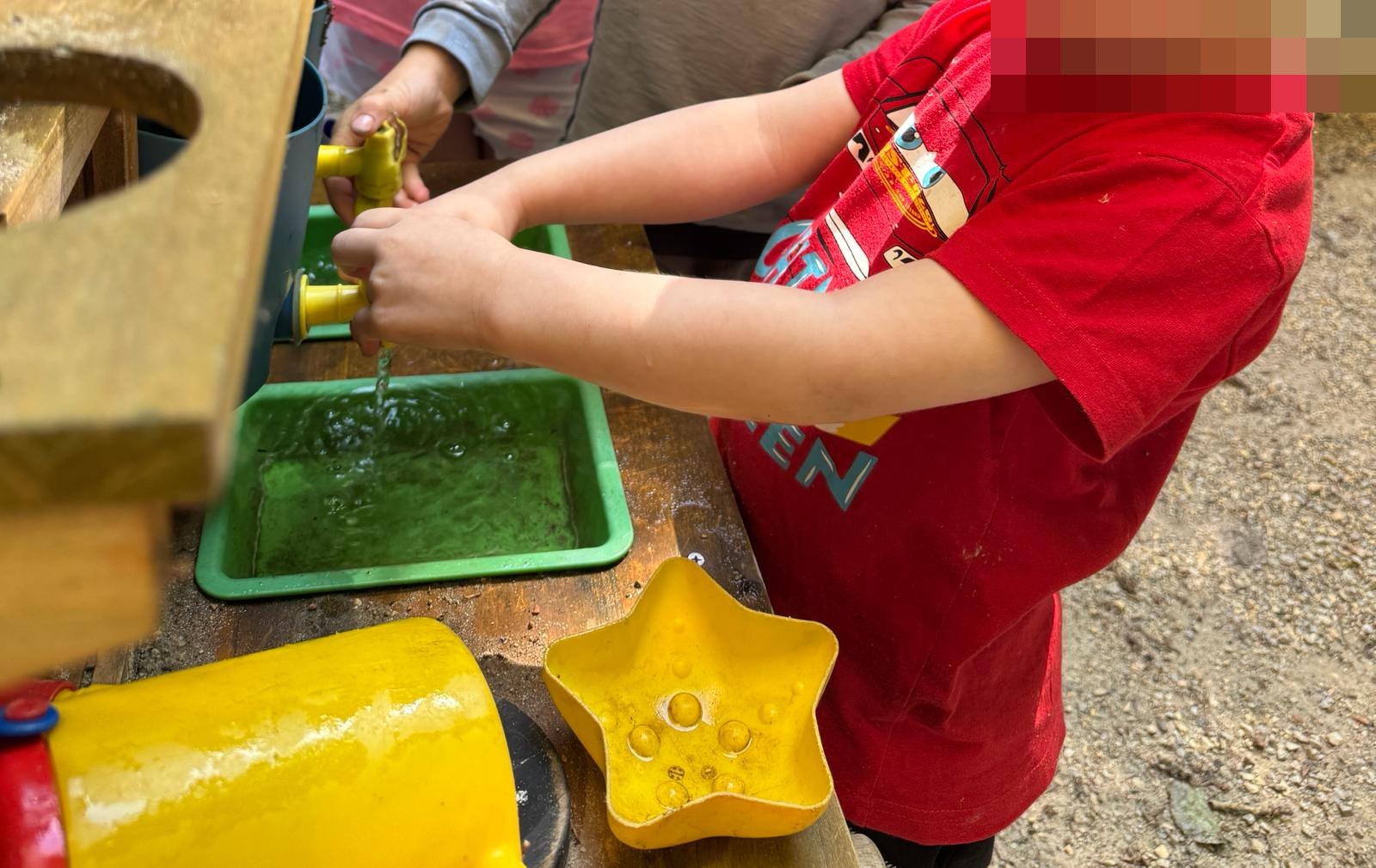 Kind spielt an der Matschküche mit Wasser