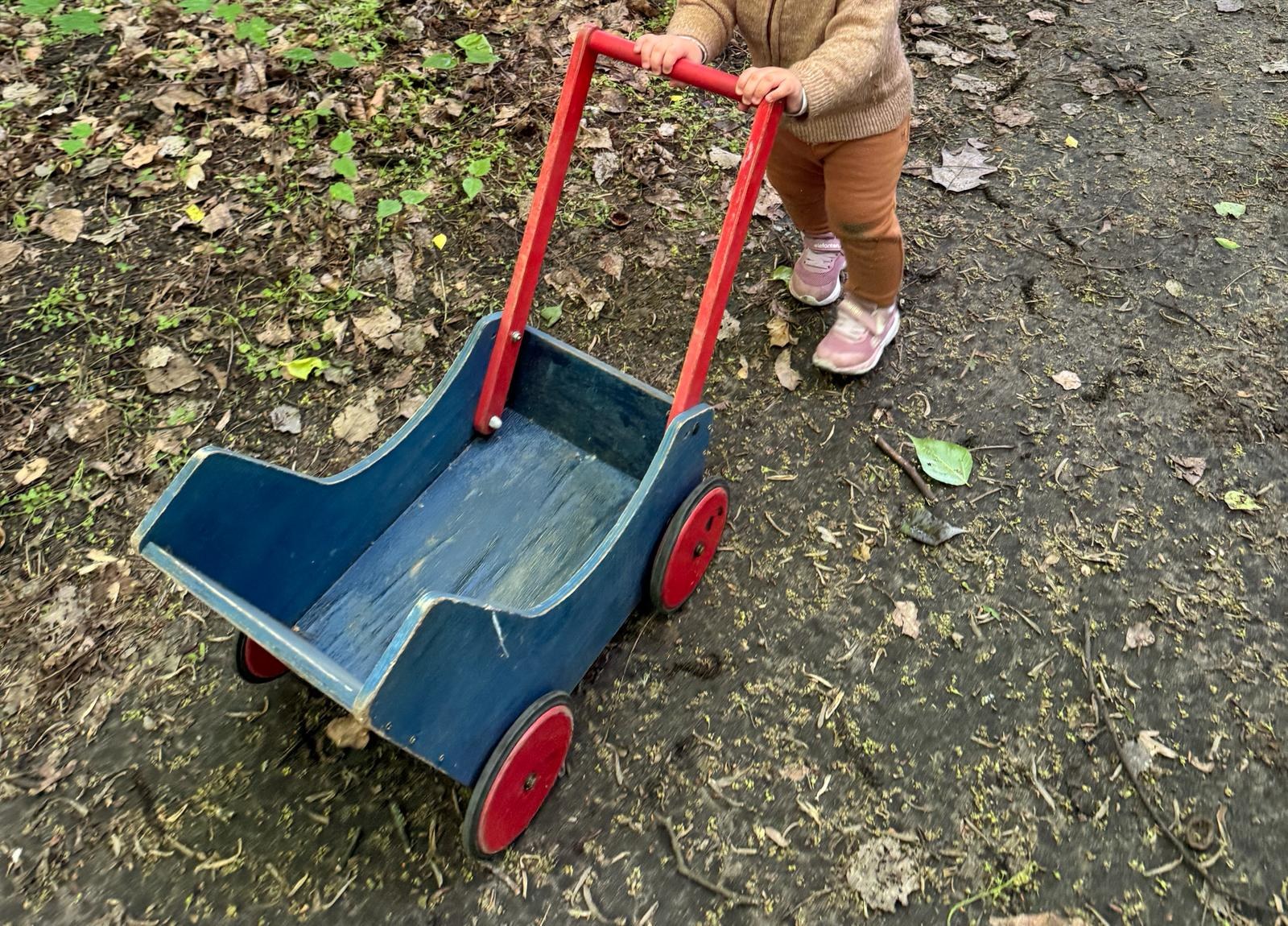 Kleinkind schiebt einen hölzernen Laufwagen durch den Garten