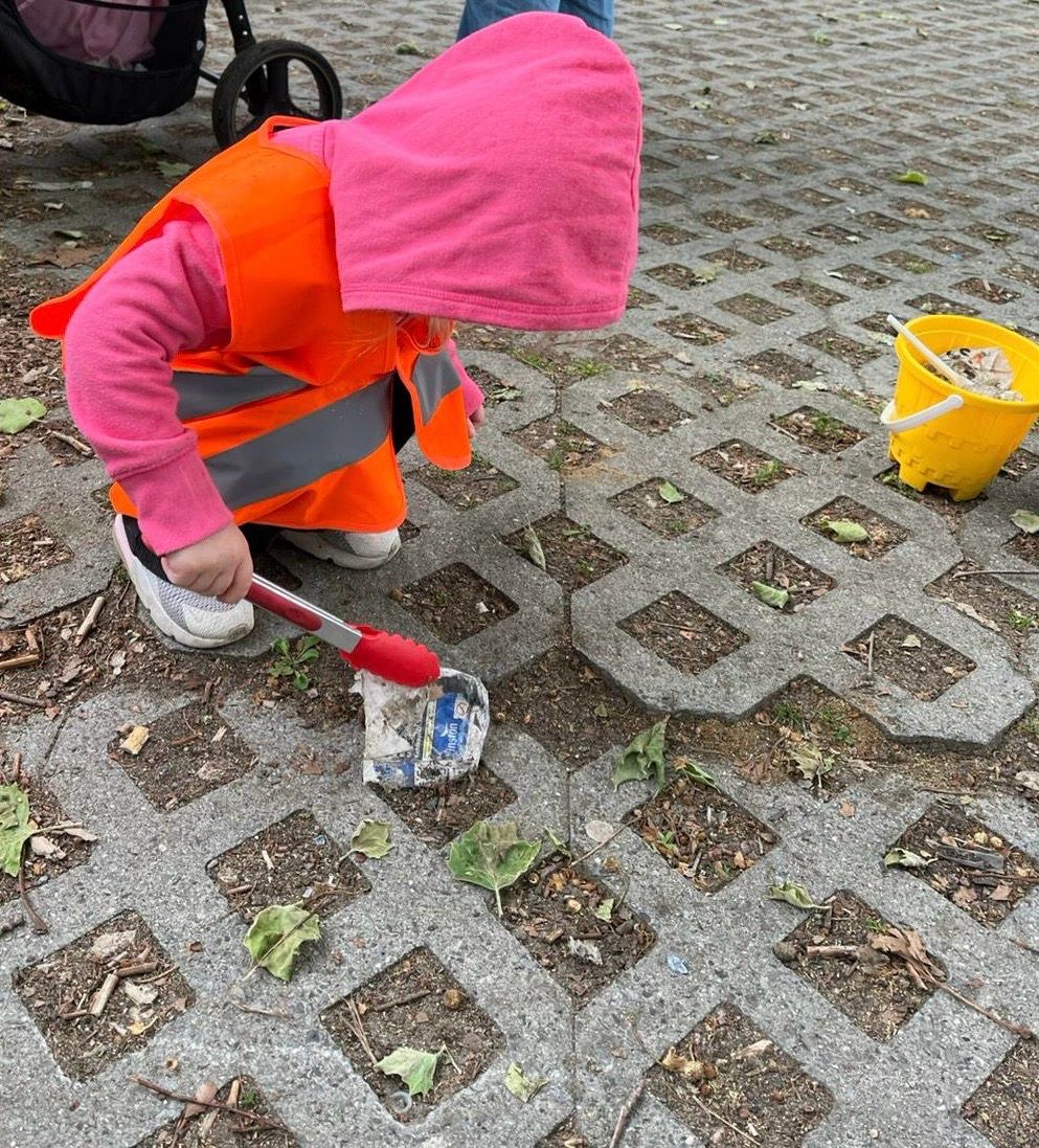 Kind in Warnweste sammelt mit einer Greifzange Müll auf