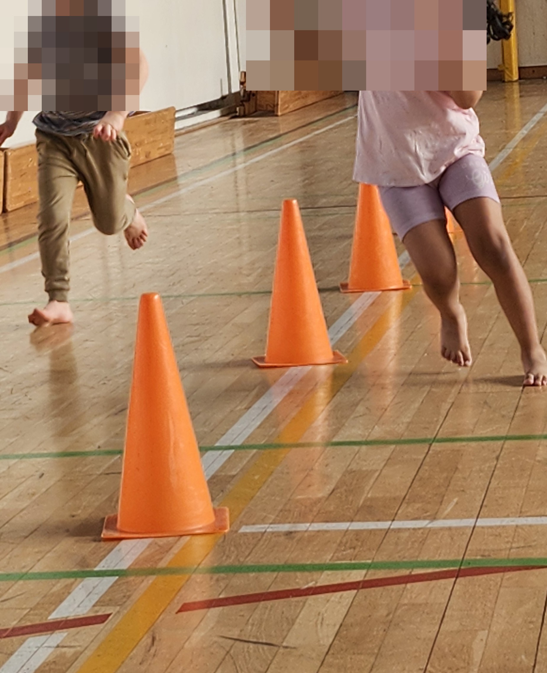 Kinder laufen einen Parcours mit Hütchen in der Turnhalle