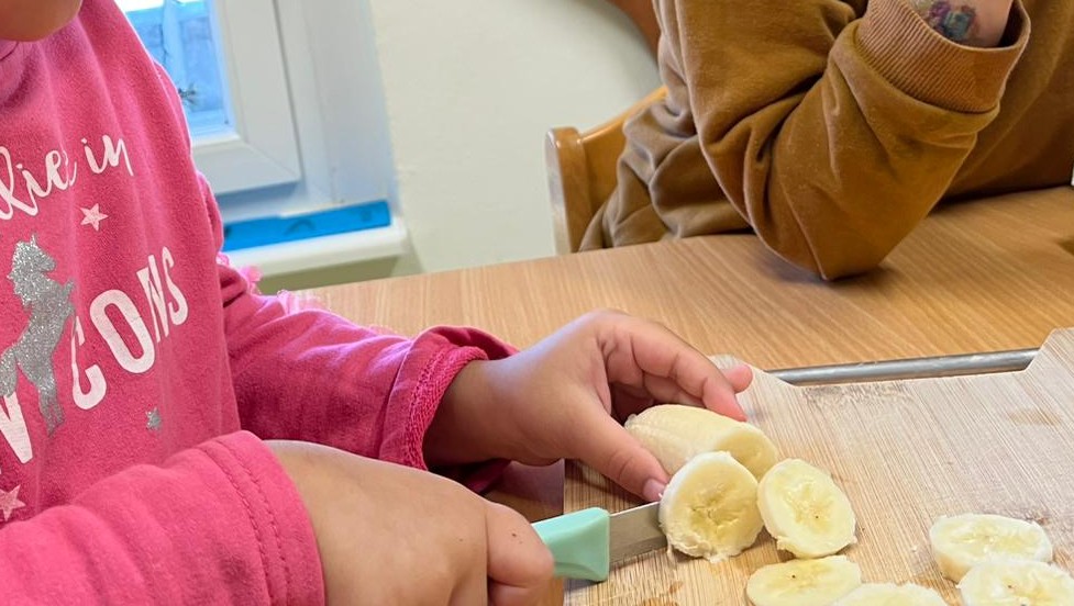 Kind schneidet selbstständig eine Banane in Scheiben